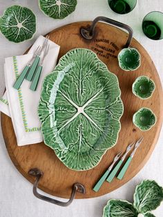 a wooden platter topped with green leafy dishes next to utensils and napkins