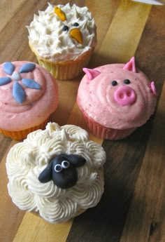 four cupcakes decorated with farm animals on top of a wooden table next to each other