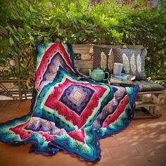 a crocheted blanket sitting on top of a wooden bench next to a potted plant