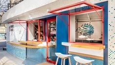 the outside of a restaurant with blue and red tiles on the walls, two stools in front of the counter