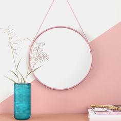 a round mirror hanging on a wall next to a vase with flowers