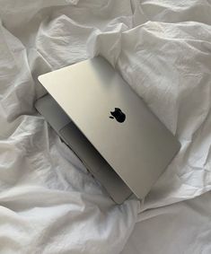 an apple laptop sitting on top of a white sheet covered bed with sheets around it