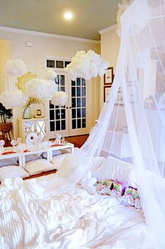 a canopy bed with white sheets and pillows in a room filled with balloons hanging from the ceiling