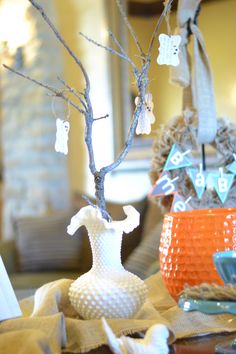 an orange vase sitting on top of a table next to a small tree with decorations hanging from it