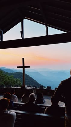 people are sitting in pews at the top of a hill with a cross on it