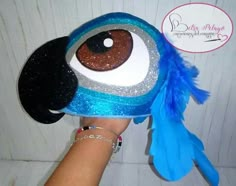 a hand holding a stuffed animal with blue feathers on it's head and eyes