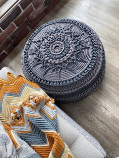 two crocheted cushions on the floor next to a brick wall and wooden floor