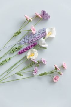 crocheted flowers are arranged on a white surface with green stems and pink ones