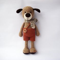 a crocheted teddy bear with an orange shorts and brown shirt is posed on a white background