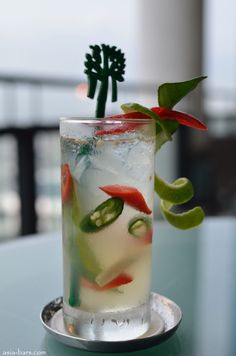 a tall glass filled with liquid and vegetables on top of a metal tray next to a plant