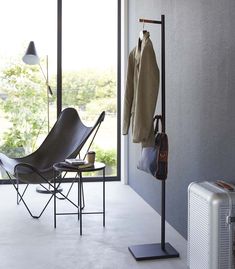 a room with a chair, coat rack and luggage on the floor next to a window