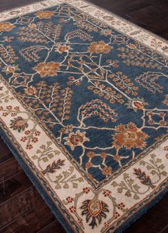 a blue and beige rug with an intricate design on the bottom, in front of dark wood flooring