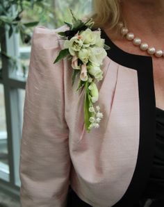 a woman wearing a pink blouse with flowers on her lap and pearls around the neck