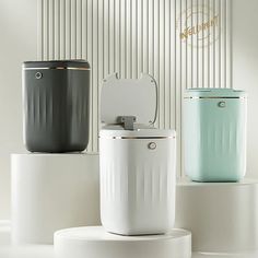 three different colored trash cans sitting on top of each other in front of a white wall