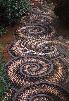 a garden path made out of rocks and stones with circular designs on the ground, surrounded by greenery