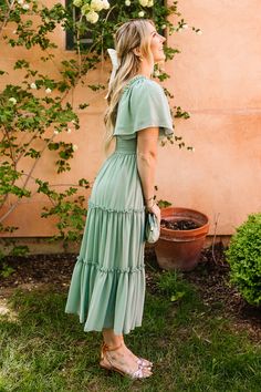 a woman standing in front of a building wearing a green dress with tiered ruffles