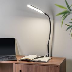 a laptop computer sitting on top of a wooden desk next to a book and lamp