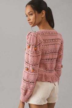 a woman wearing a pink crochet sweater and white shorts is looking off to the side