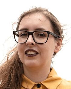 a woman wearing glasses and a yellow shirt is looking off to the side with her hair blowing in the wind