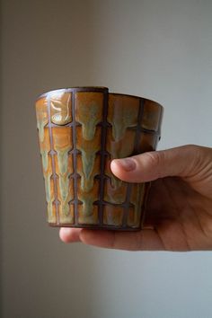 a hand holding a cup that is made out of clay and has designs on it