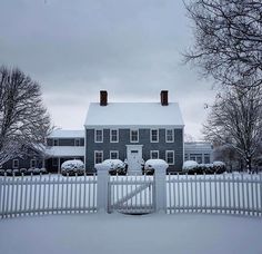 a white picket fence is in front of a large house with snow on the ground