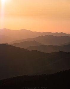 the sun shines brightly in the distance over some hills and mountains as seen from an overlook point