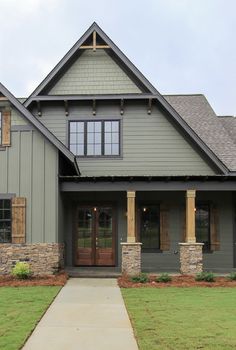 a gray house with brown trim and stone pillars on the front door, along with green grass