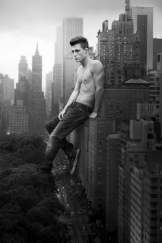 a shirtless man sitting on top of a tall building