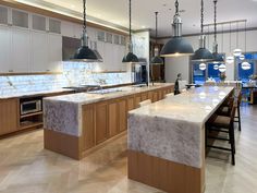 a large kitchen with marble counter tops and wooden cabinets, along with pendant lights hanging from the ceiling