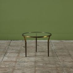 a glass table sitting on top of a cement floor in front of a green wall