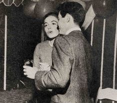 an old black and white photo of a man kissing a woman in front of balloons