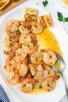 a white plate topped with shrimp next to toasted bread and parsley on the side