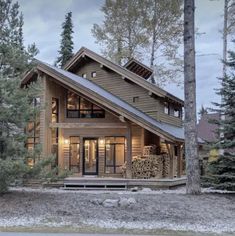 a small cabin style house with lots of windows and wood on the front, surrounded by pine trees