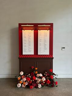 two red and white flowers sitting in front of a wall with menus on it