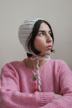 a woman wearing a pink sweater and a white knitted hat with buttons on it