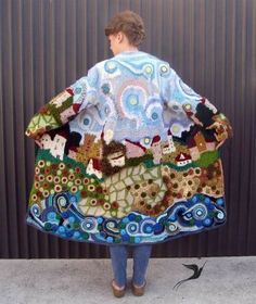 a woman wearing a colorful jacket with houses and clouds on it, standing in front of a metal wall