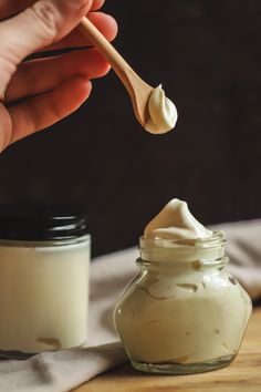 a hand holding a spoon over a jar filled with whipped cream