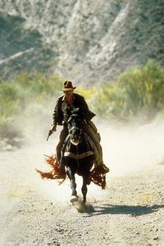 a man riding on the back of a horse down a dirt road