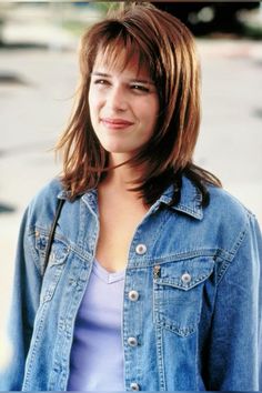 a woman in a jean jacket standing on the street smiling at the camera with her hands behind her back