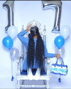 a woman with long hair sitting in a chair surrounded by blue and silver balloons, holding a handbag