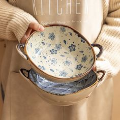 a person holding two bowls in their hands and the bowl has blue flowers on it