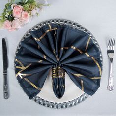 a place setting with black napkins, silverware and pink flowers on the table