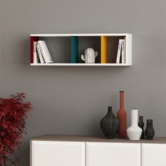 two white shelves with books and vases on them against a gray wall next to a potted plant