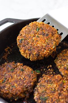 three burger patties being cooked in a skillet with a spatula on top