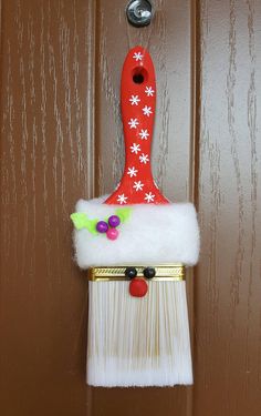 a red and white christmas decoration hanging on a brown door with a brush attached to it