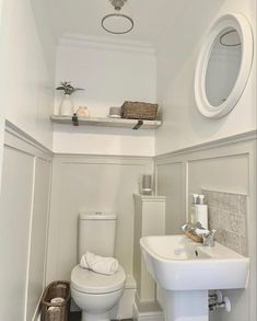 a white toilet sitting next to a sink in a bathroom under a mirror and shelf above it