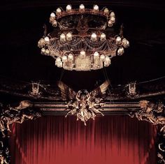 an ornate chandelier hangs from the ceiling in front of a stage with red curtains