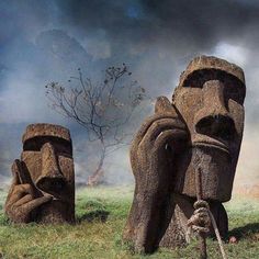 two large statues in the grass with trees and clouds behind them on a cloudy day