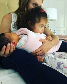 a woman holding a baby in her arms while sitting on a bed with another child