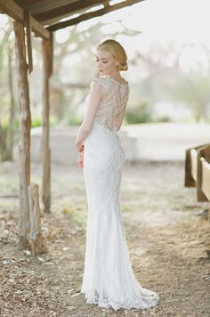 a woman in a white wedding dress standing under a wooden structure with her back to the camera